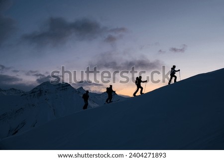 Silhouettes of four skiers on the highest point of the mountain against the background of the mountain peaks in the fog and the red sky Royalty-Free Stock Photo #2404271893