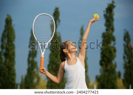 Girl tennis school age in a suit with a racket and a ball shows the elements of the sport. Open Park area. The concept of sport and healthy lifestyle.