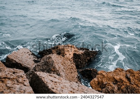 Mediterranean winter stormy seaside. Close up water with stones on the beach concept photo. Underwater rock with algae. The view from the top, nautical background. 