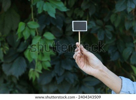 Hand holding Chalkboard label, blank wooden blackboard tag, garden sign on green leaves wall background