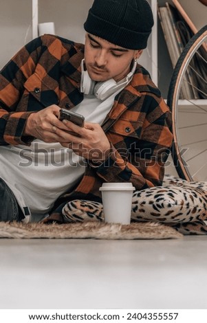 young man at home with mobile phone sitting on the floor wearing hat and autumn winter clothes