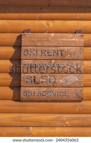 Brown wooden planks information board. Ski center resort services. Ski rent, sled and snowboard. Black letters, symbols. Words.
