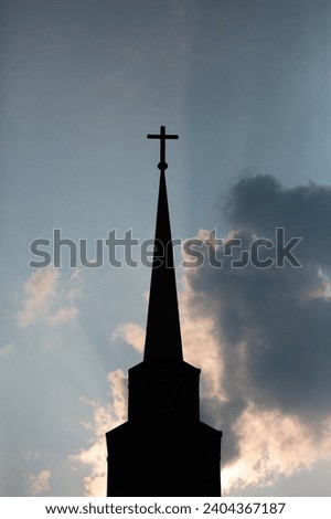 Cross and church steeple with sun lighting it and blue sky in the background, vertical