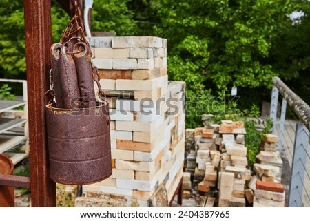 Rusty Bucket and Bricks at Construction Site with Greenery Background Royalty-Free Stock Photo #2404387965