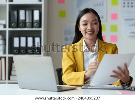 Asian businesswoman, investor, insurance salesperson pointing at data sheet. Earnings. Chart showing financial growth in real estate business based on data from laptop. Modern working lifestyle.