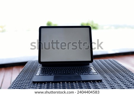 blank screen of tablet computer on outdoor rattan table with swimming pool background.