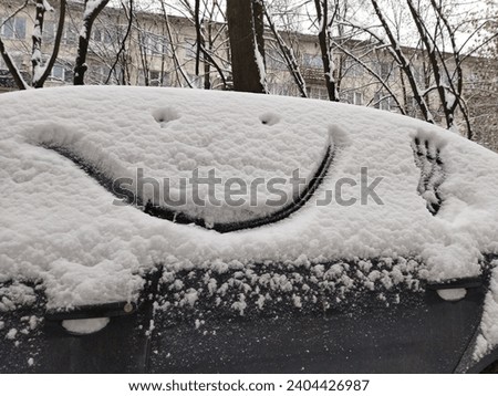 Face with a smile is painted on a car covered with snow in winter. Funny close up drawing, frosty humor pattern. Royalty-Free Stock Photo #2404426987