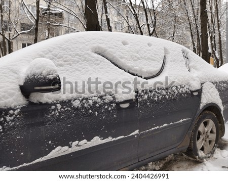 Face with a smile is painted on a car covered with snow in winter. Funny close up drawing, frosty humor pattern. Royalty-Free Stock Photo #2404426991