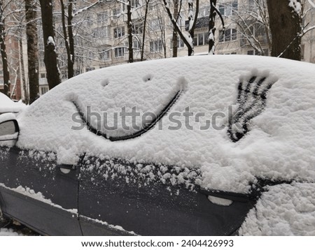 Face with a smile is painted on a car covered with snow in winter. Funny close up drawing, frosty humor pattern. Royalty-Free Stock Photo #2404426993