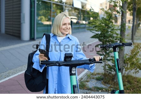 Portrait of young woman, renting a scooter, using mobile phone app to unlock it, using quick ride to get to work, smiling and looking happy.