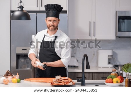 Millennial hispanic man in chef apron and cook hat hold salmon fillet at kitchen. Cooking salmon fillet. Restaurant menu with salmon fillet. Cooking, advertising salmon fillet concept.