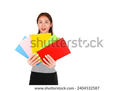 Surprised young female asian teacher holding different coloured notebooks against a white background