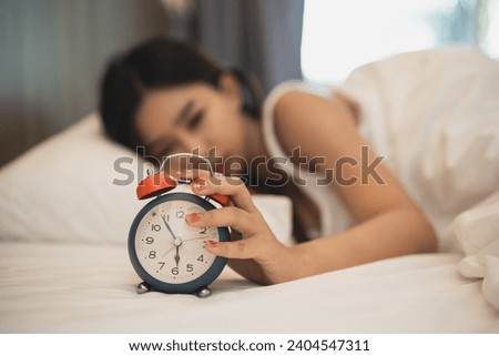 Close up alarm clock. woman sleeping in comfortable bed with silky linens in the morning. Women lying in bed and keeping eyes closed while covered with blanket. cheerful and comfortable.