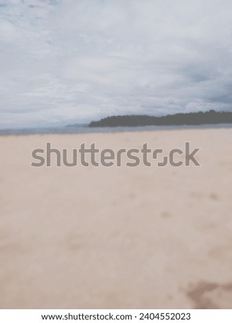 Blurry beach. Beach panorama with blurred red beach sand, coastline and green hills stretching horizontally. Focus on blue sky with sparkling white clouds.