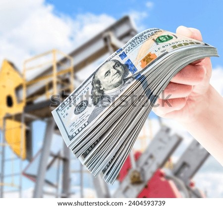 American dollars in the hand against the oil pump jack extraction machine. Buying and selling oil for dollars. Oil industry equipment and finance