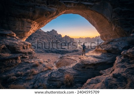 a man standing in a cave at sunset Natural rock bridge in the Hisma Desert NEOM, Saudi Arabia Royalty-Free Stock Photo #2404595709