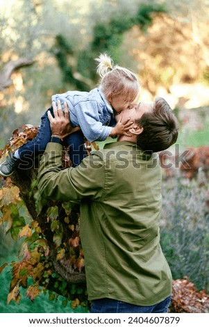 Little girl kisses her dad leaning towards him from a tree in the park