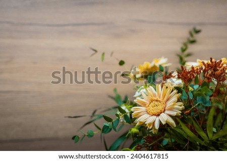Autumn floral bouquet on light brown background. Big yellow flower and green leaves, plenty of copy space for text. Beautiful floral image.