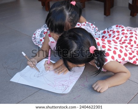 This picture shows the twin are drawing together. they wear the same dress and tied hair. They try to finish it while laughing to each other.