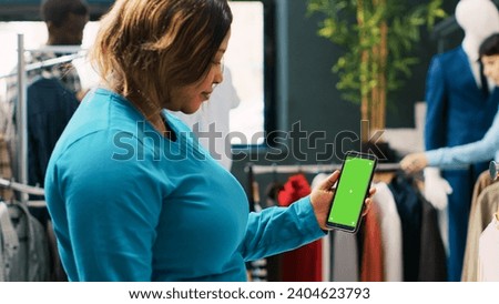 African american customer holding mobile phone with green screen display, checking clothing store app. Stylish woman shopping for fashionable clothes and trendy accessories in modern boutique