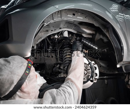 An auto mechanic applies anti-corrosion mastic to the underbody of a car. Royalty-Free Stock Photo #2404624359
