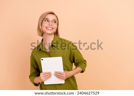Photo of clever woman with bob hairstyle dressed green shirt hold tablet look at offer empty space isolated on beige color background