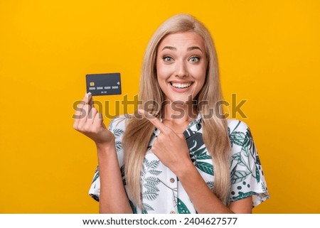 Photo of overjoyed impressed girl with long hair dressed print shirt indicating at credit card isolated on yellow color background