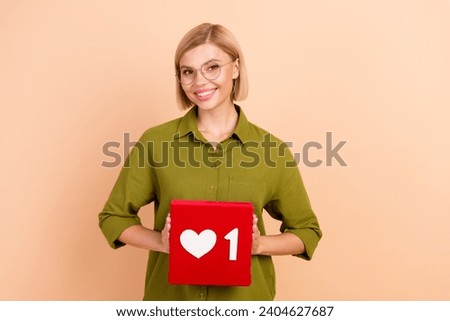 Photo of optimistic gorgeous woman with bob hairstyle in glasses holding social media like box in arms isolated on beige color background