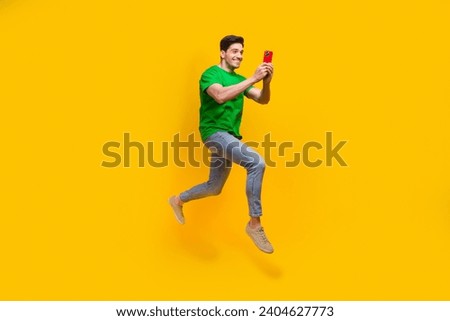 Full length photo of cheerful positive man dressed green t-shirt run look at smartphone take picture isolated on yellow color background