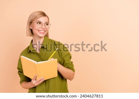 Photo of clever positive woman dressed green shirt in glasses write notebook look at promo empty space isolated on beige color background