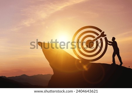 Silhouette of businessman pushing a target board on top of the hill. Concept of aim and objective achievement, striving for success. Royalty-Free Stock Photo #2404643621
