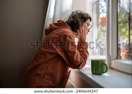 Introverted teenager spending time alone at home in warm sunny day, looking at window indifferently. Unsociable teen girl in puberty crisis with absence of life motivation, apathy, loss of interest Royalty-Free Stock Photo #2404644247