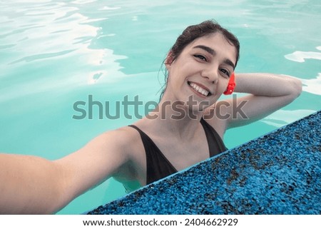 A smiling young dark-haired woman bathes in a hot thermal spring on a winter day.A woman takes pictures of herself on her smartphone.Self-care,healthy lifestyle,leisure activity,mental health concept.