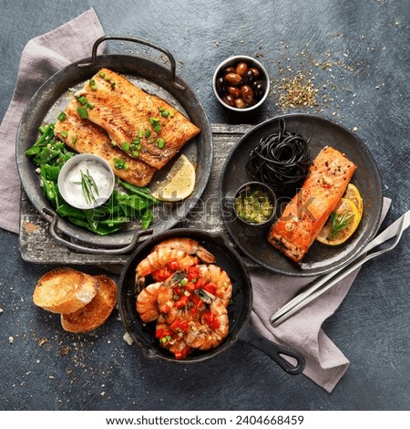 Grilled salmon fish fillet with lemon and strimps. Sea food dishes assorty. Healthy concept. Top view Royalty-Free Stock Photo #2404668459