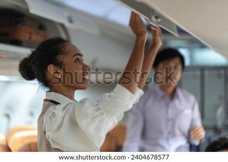 Flight attendants check that lockers above passenger seats on airplanes are closed before takeoff. Royalty-Free Stock Photo #2404678577