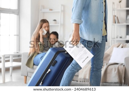 Young man with divorce decree and suitcase leaving his family at home Royalty-Free Stock Photo #2404689613