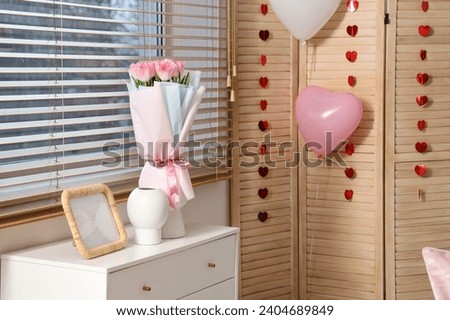 Vases with roses and blank frame on drawers in room decorated for Valentine's Day