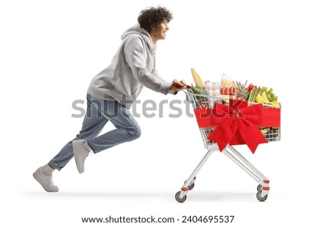 Young man running with christmas food in a shopping cart isolated on white background