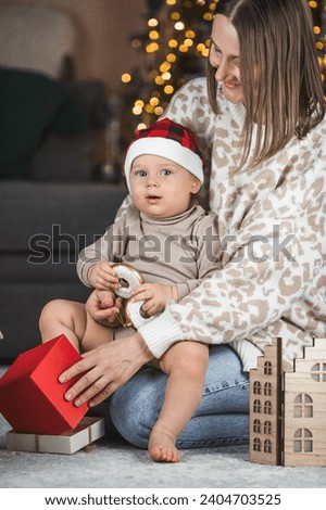 Family. A beautiful little blond boy of 1 year old is sitting with his mother on the background of a Christmas tree. The concept of celebrating Christmas and New Year 2024.