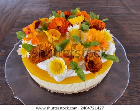 Mango cheesecake decorated with orange and yellow flowers and green herbs on a glass platter 