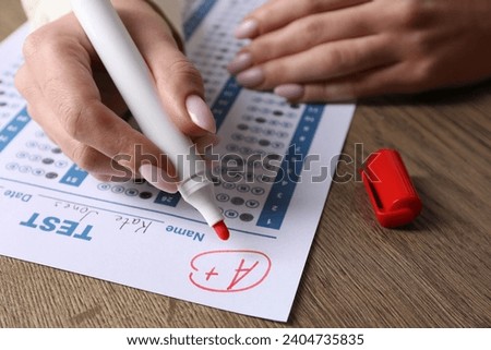 School grade. Teacher writing letter A with plus symbol on answer sheet at wooden table, closeup Royalty-Free Stock Photo #2404735835
