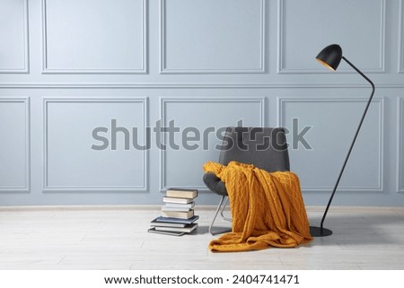 Comfortable armchair with blanket, books and lamp near grey wall indoors, space for text