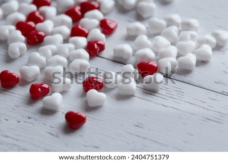 A vibrant pile of glossy red and white hearts spills across a rustic wooden table in this close-up shot.