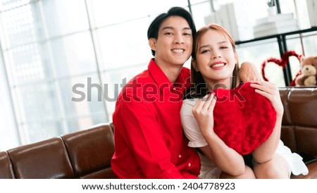 A young happy Asian couple looking at the camera, sitting, embracing and smiling on Valentine's Day at home. Asian woman enjoys her anniversary date with her boyfriend. Valentine's Day celebration.