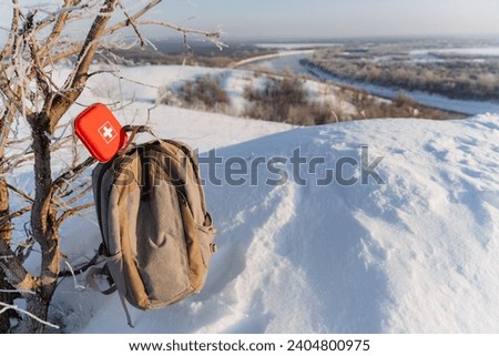 Hiking backpack hanging on a branch against the background of a winter forest, a red first aid kit on a hiking trip, a beautiful morning landscape in winter in the mountains. High quality photo
