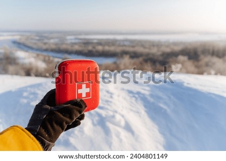 A first aid kit in a man's hand against the background of a winter landscape, a hike in a winter forest, a red box with medicines. High quality photo