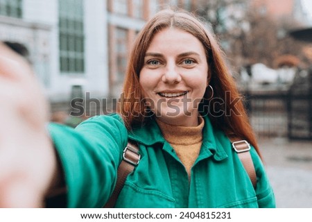 Happy 30s Women taking selfie on urban background. Young beautiful girl with backpack say Hi. Gdansk old town. Urban lifestyle concept.