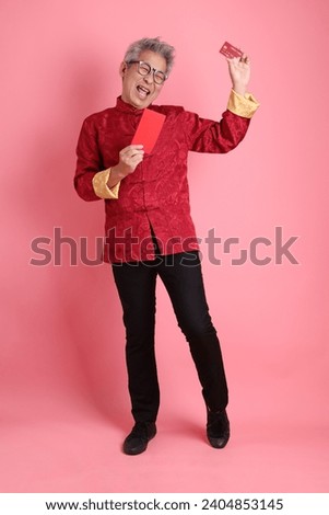 Happy Chinese new year. Asian Chinese senior man wearing red traditional cheongsam qipao dress with gesture of holding Chinese Red envelopes and bank credit card isolated on pink background.