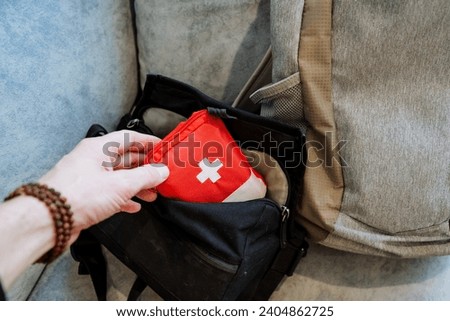 A person takes a small first-aid kit with medicines with him on the road, puts a red first-aid kit in the pocket of his bag. High quality photo