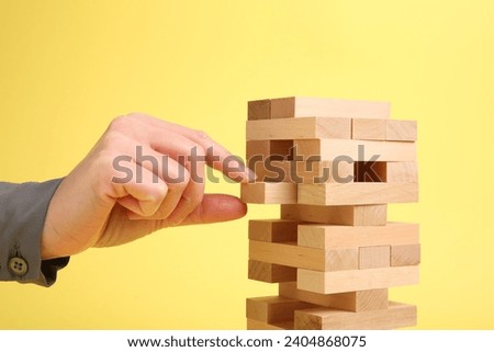 Woman playing Jenga tower on yellow background, closeup